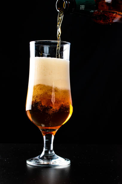 istock Beer is pouring into a glass from bottle on black background 1127254393
