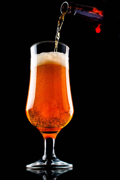 istock Beer is pouring into a glass from bottle on black background 1127254415