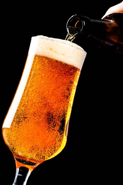 istock Beer is pouring into a glass from bottle on black background 1127254418