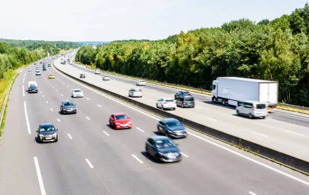 Heavy but fluid traffic on the eight-lane A10 highway in France in the direction of Paris by a hot summer day with cars, vans, trailers and semitrailer truck driving.