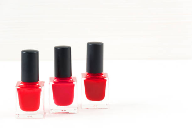close-up image of three red nail polish bottles on white wooden background. - pampering nail polish make up spilling imagens e fotografias de stock