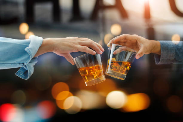 ウィスキー飲むアルコール飲料でカラフルな背景の仕事の後パブでカウンター バーながら一緒に 2 人の男性チャリンという音メガネのクローズ アップ - thailand restaurant cocktail bar ストックフォトと画像