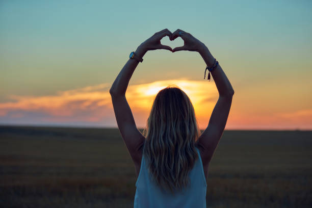 chica sosteniendo el símbolo de forma de corazón para el amor en el atardecer / tiempo del amanecer. - heart shape loneliness women praying fotografías e imágenes de stock