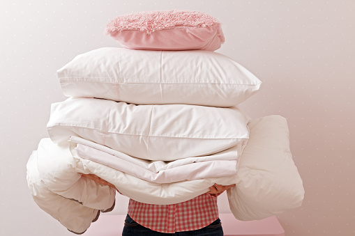 Woman holding a pile of bedding for sleeping. Household