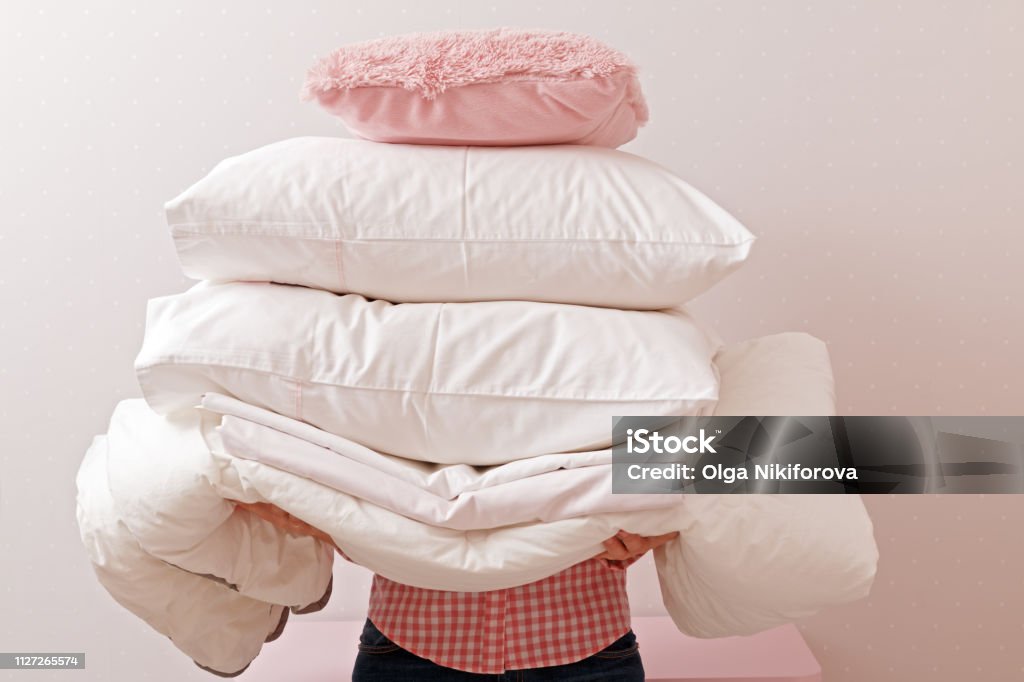 Woman holding a pile of bedding for sleeping. Household Pillow Stock Photo