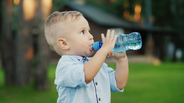 The little boy has been drinking water from the bottle for 1 year. Standing in the backyard of your house stock photo