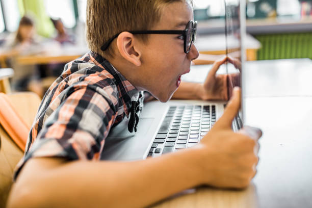 Shocked nerdy schoolboy e-learning over laptop in the classroom.