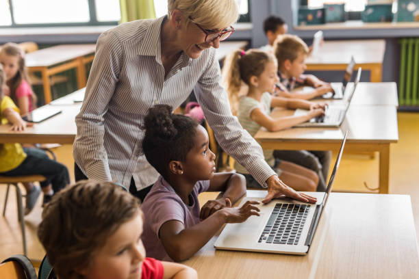 istock Happy mature teacher assisting school kids in using computers on a class. 1127269650