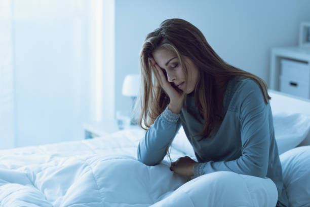 Depressed woman awake in the night, she is touching her forehead and suffering from insomnia stock photo