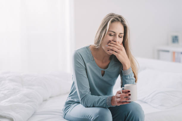 verschlafene faule frau einen kaffee, sie sitzt auf dem bett und gähnen - yawning stock-fotos und bilder