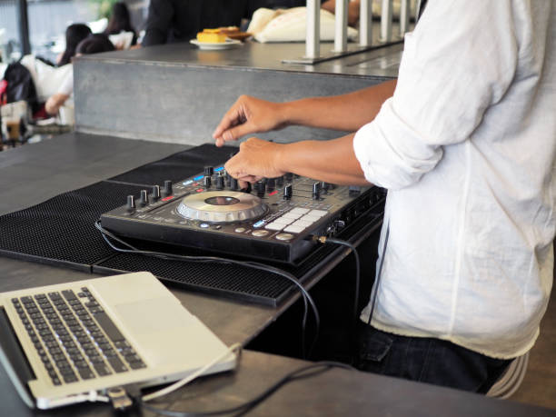 Disc jockey plays music by using digital disc and computer, entertaining people in the cafe.