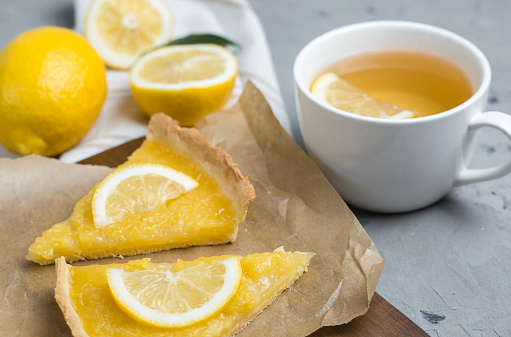 two pieces of lemon tart with slice of lemons closeup on stone background