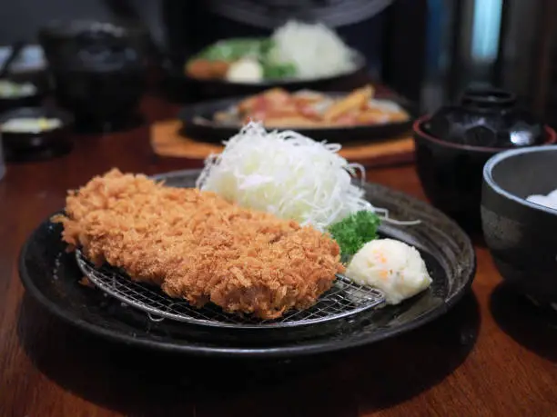 Photo of Homemade Japanese deep fried breaded pork tenderloin or cutlet served with shredded cabbage dipped with tonkatsu sauce. Japanese traditional food.