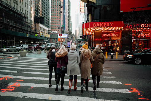 A rear-view shot of a group of women walking down a road in New York City, they are having fun together and they are wearing warm clothing.