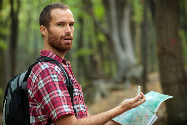 istock Happy young man holding a map and navigational compass, orienteering in a forest 1127274420