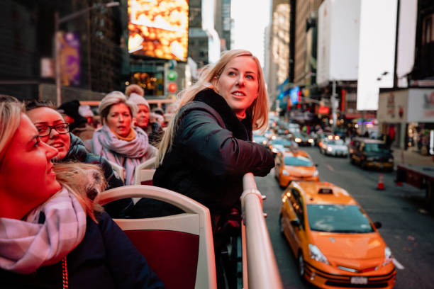 A front-view shot of a group of women on a open top bus tour in New York City, they are sightseeing and having fun together, they are wearing warm clothing.