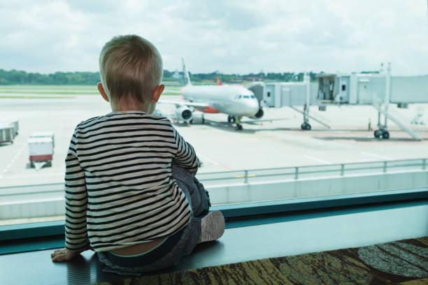 в зале аэропорта ребенок смотрит на самолет через окно - baby holding babies only sign стоковые фото и изображения
