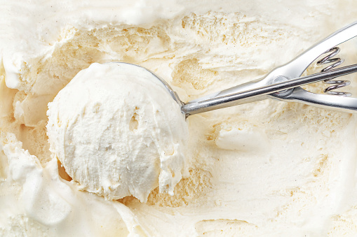 Vanilla ice cream with a scoop in  container as background. Macro. Scooped out ice-cream,  top view.