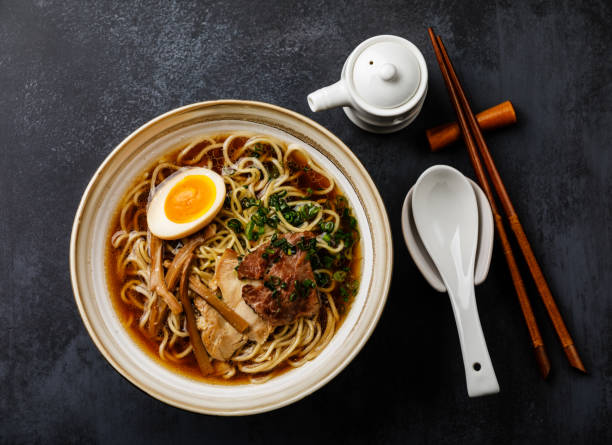Ramen asian noodle in broth with meat and Ajitama pickled egg in bowl on dark background stock photo