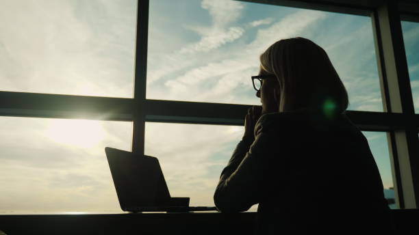 uma mulher em um terno de negócio olha pela janela de seu escritório. conceito - olhar em frente no negócio - apartment window sky sun - fotografias e filmes do acervo