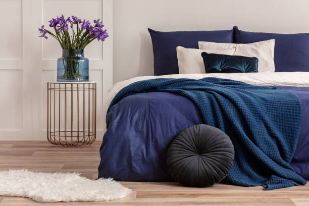 istock Flowers in vase on stylish nightstand table next to comfortable bed with white and blue bedding 1127298979