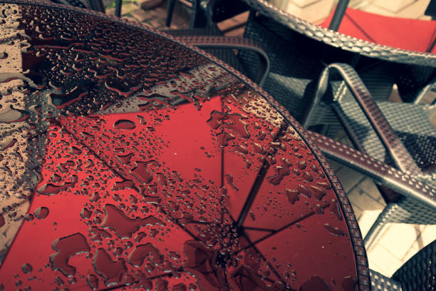 Table in the summer cafe with water drops Glass table in a summer cafe with water drops and a reflection of a red umbrella next to metal wicker chairs rainy cafe stock pictures, royalty-free photos & images