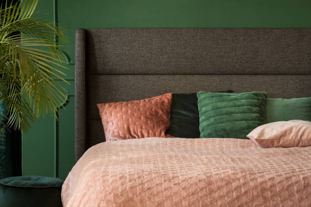 istock Pastel pink and emerald bedding on comfortable king size bed with headboard, copy space on empty wall 1127302973