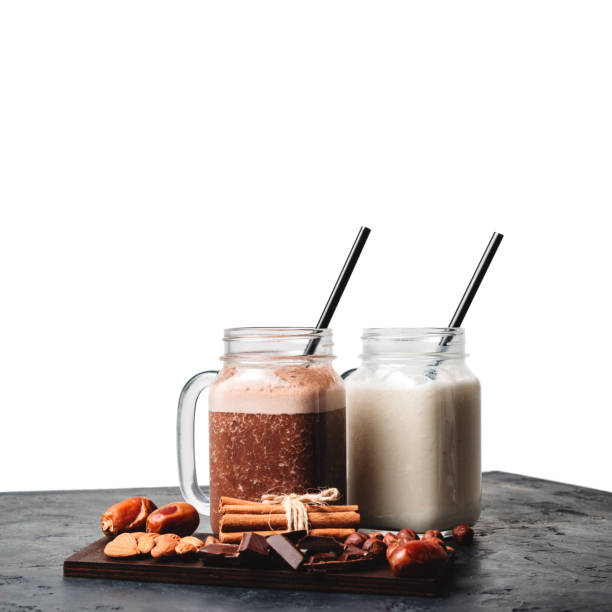 istock Banana and chocolate smoothie in two jars, protein milkshake, nuts, chocolate cubes, dates, cinnamon sticks on a dark table isolated on white background 1127304679