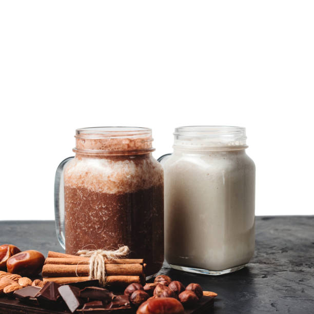 istock Banana and chocolate smoothie in two jars, protein milkshake, nuts, chocolate cubes, dates, cinnamon sticks on a dark table isolated on white background 1127304681