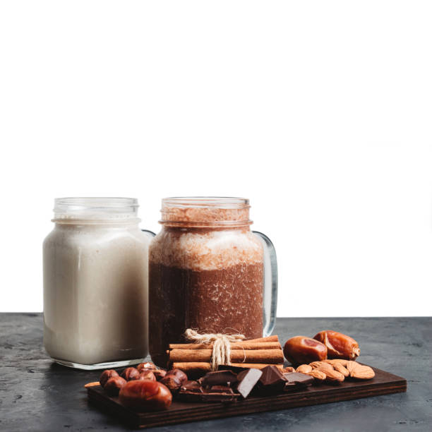 istock Banana and chocolate smoothie in two jars, protein milkshake, nuts, chocolate cubes, dates, cinnamon sticks on a dark table isolated on white background 1127304695