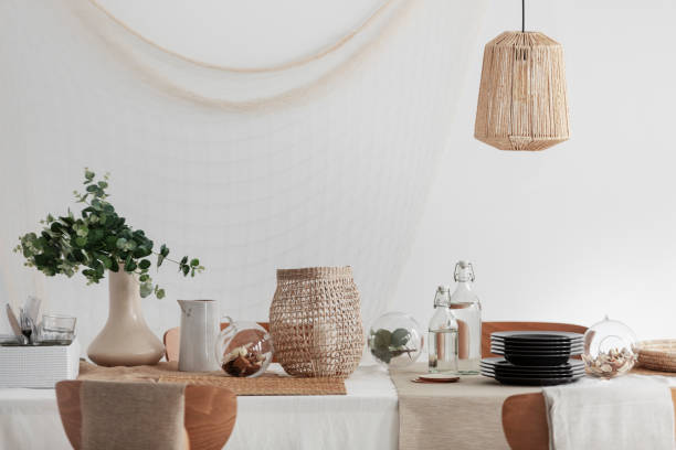 istock Green plant in beige vase, white jug and wicker lantern on dining table in bright interior 1127306504