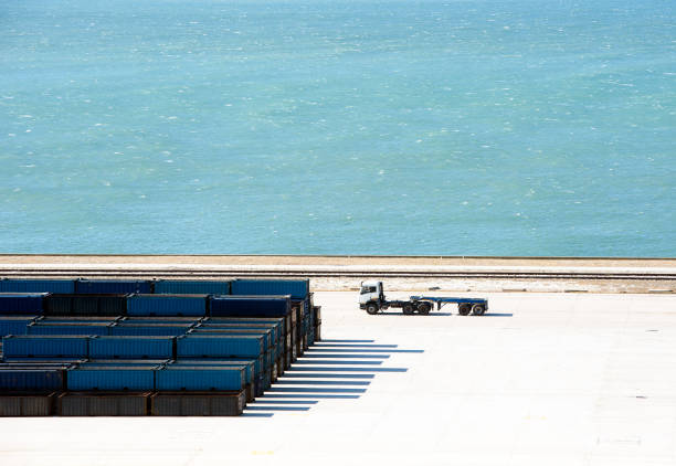 Containers stacked along the quay, or dockside, create graph-like shadows prior to loading the freight onto flat bed articulated semi lorries for onward transportation, with the sea as backdrop in the harbour of Port Elizabeth, South Africa