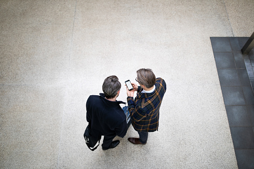 Shot from above of two traveling businessmen standing together outdoors and using mobile phone. Business travelers using navigation app on the smartphone on street.