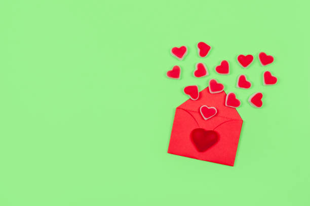 istock Valentines day pastel minimal creative background. Text Love is, red envelope many heart shape candies on green background. Valentines day, Love, romance concept 1127312845