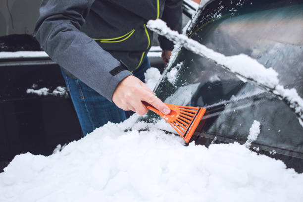 istock Man cleaning car from snow and ice with brush and scraper tool during snowfall. Winter emergency. Weather-related vehicle emergencies. Automobile covered with snow 1127312934