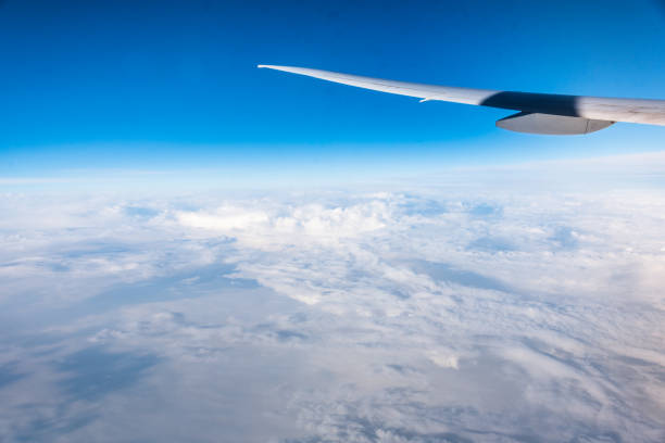 Wing of an airplane flying above the clouds with blue sky. View at the sky from the window of the plane.