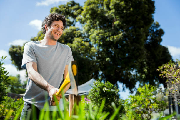 Smiling man cutting logs with axe on sunny day