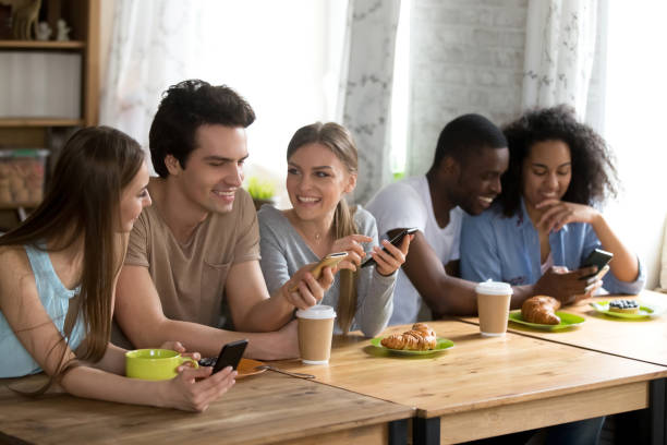 istock Happy smiling friends sitting together in cafe, using phones 1127327152