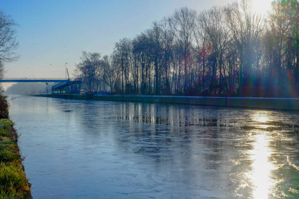 Beautiful early winter landscape with a frozen river or canal, treelined riverside and grass at sunrise creating a tranquile and quiet scenic nature background