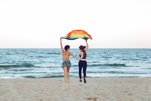 Young female couple with rainbow flag at the beach