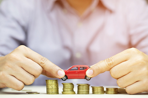 Business man in suit and close up hand holding model of toy car red on over a lot money of stacked coins - insurance, loan and buying car finance concept. isolated white background.