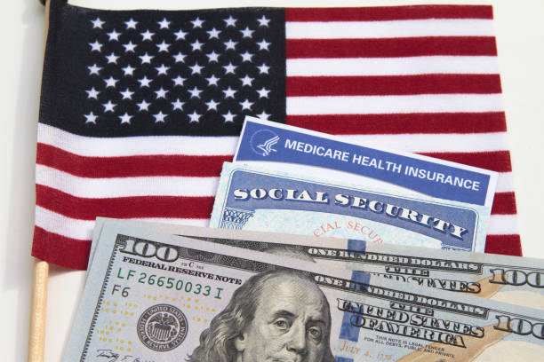 Government benefits: Social Security card and Medicare card on USA flag Government benefits: Social Security card and Medicare card on USA flag along with two hundred dollar bills. social security social security card identity us currency stock pictures, royalty-free photos & images