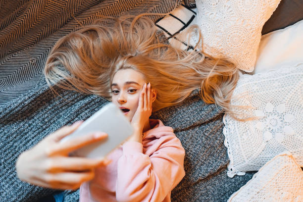 istock Surprised young girl, making selfie with smart phone while lying on the bed at home 1127350664