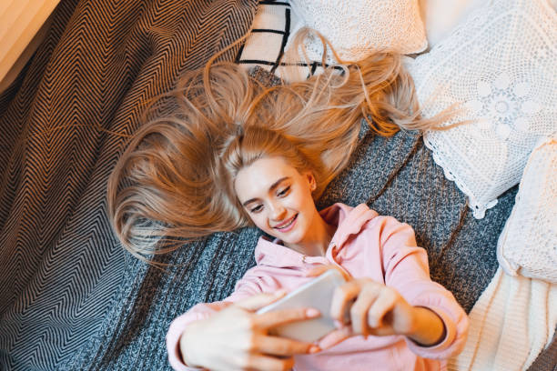 istock Pretty young girl having fun, making selfie with smart phone while lying on the bed at home 1127350667