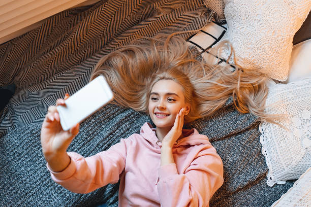 istock Pretty young girl having fun, making selfie with smart phone while lying on the bed at home 1127350680