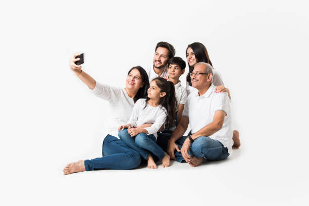 istock Indian family taking selfie picture with smartphone while sitting on white background includes 3 generations. selective focus 1127353975