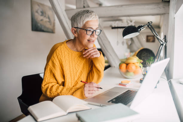 Older woman working on laptop Smiling senior woman with computer at home e learning stock pictures, royalty-free photos & images