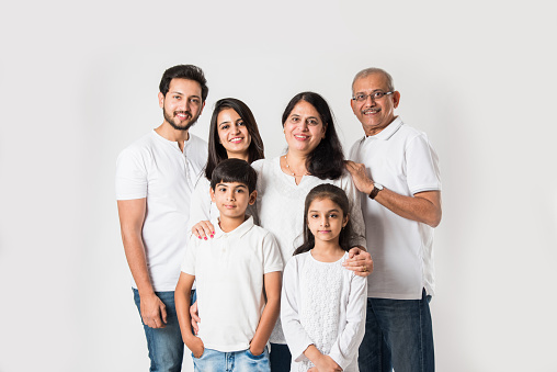 Indian family standing isolated over white background. senior and  young couple with kids wearing white top and blue jeans. selective focus