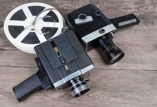 Different vintage amateur movie cameras and films on wooden surface Two old vintage amateur film movie cameras powered by clockwork motor and electric motor and reels of motion picture films Super 8mm format on an old wooden surface vintage amateur movie camera stock pictures, royalty-free photos & images