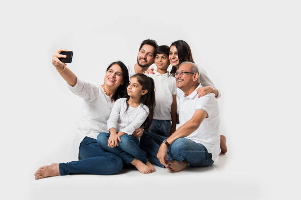 família indiana tirando foto de selfie com smartphone enquanto está sentado no fundo branco inclui 3 gerações. foco seletivo - wireless technology cheerful granddaughter grandmother - fotografias e filmes do acervo